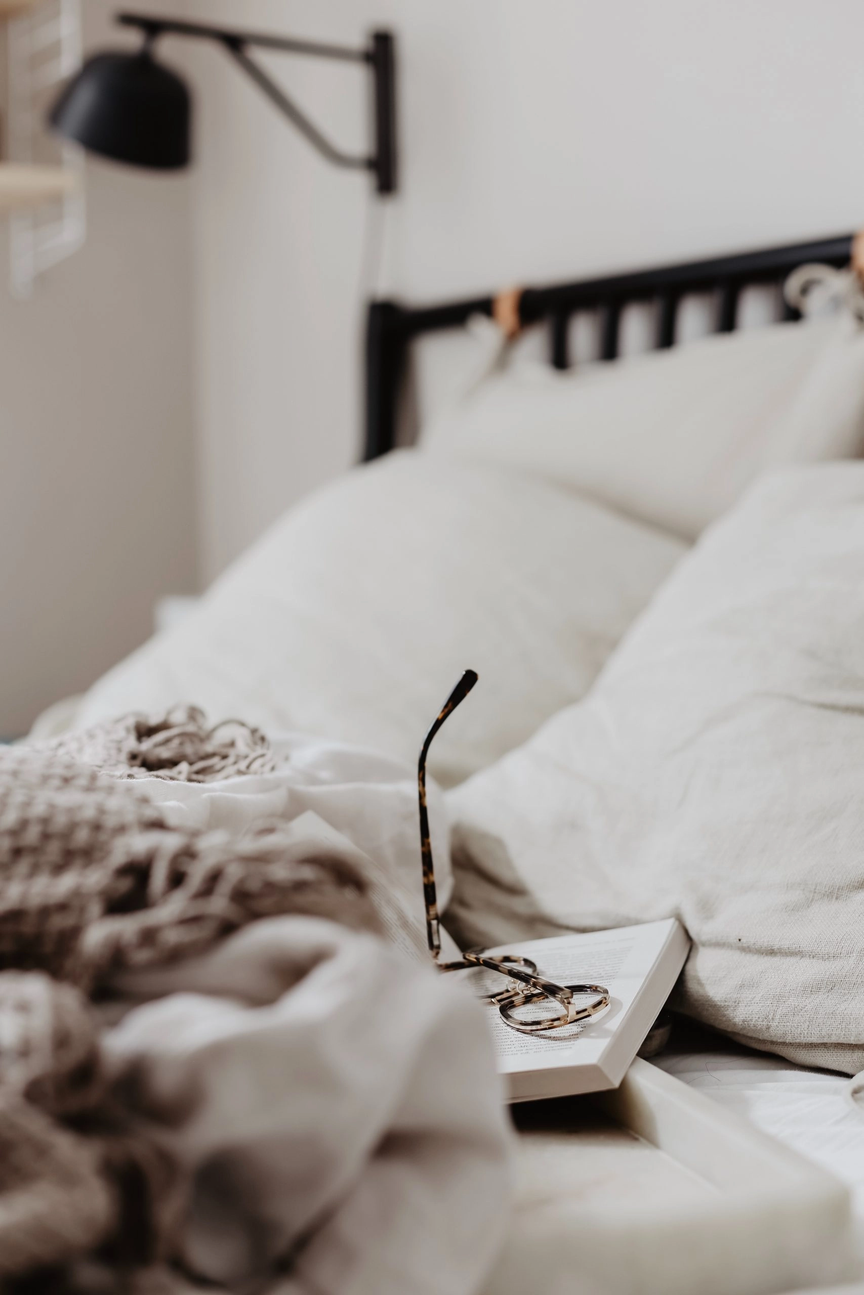 Lit paisible avec livre ouvert et lunettes de lecture posé sur les couvertures