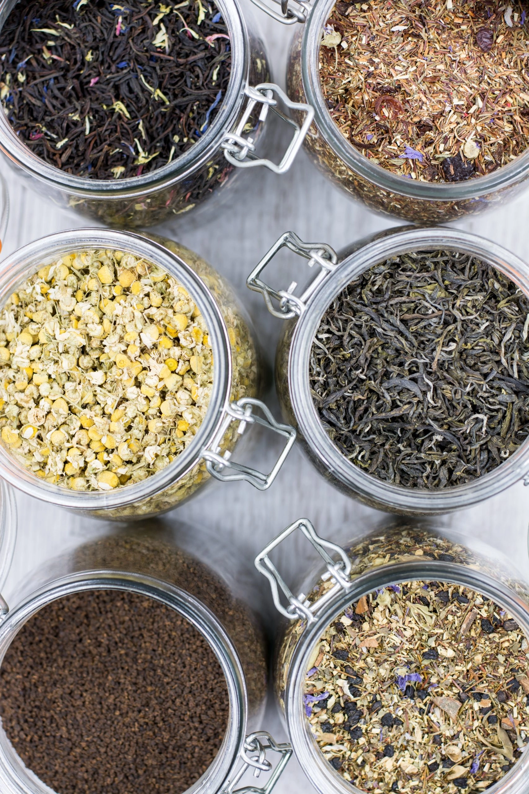 six pots hermétiques en verre avec différentes plantes séchés : camomille, thé et tisanes