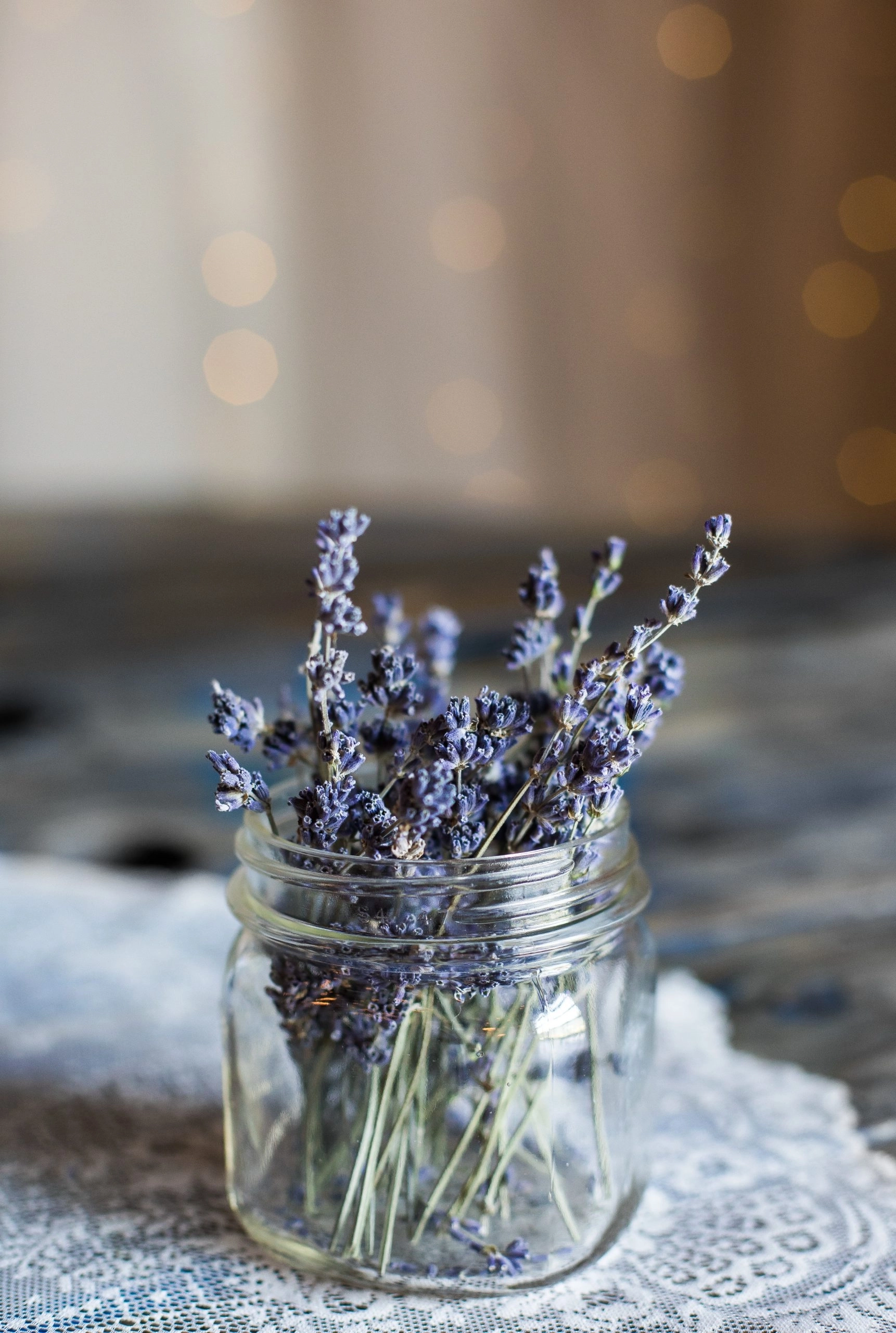 Pot en verre avec petites tiges de lavande sur une table couverte d'un joli naperon en dentelle blanche.