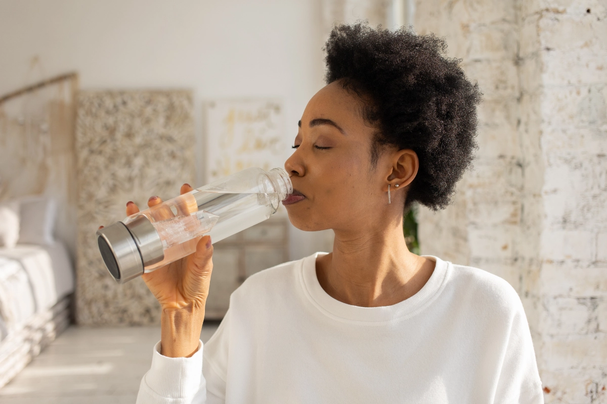 Femme qui boit dans une bouteille d'eau en verre, les yeux fermés.