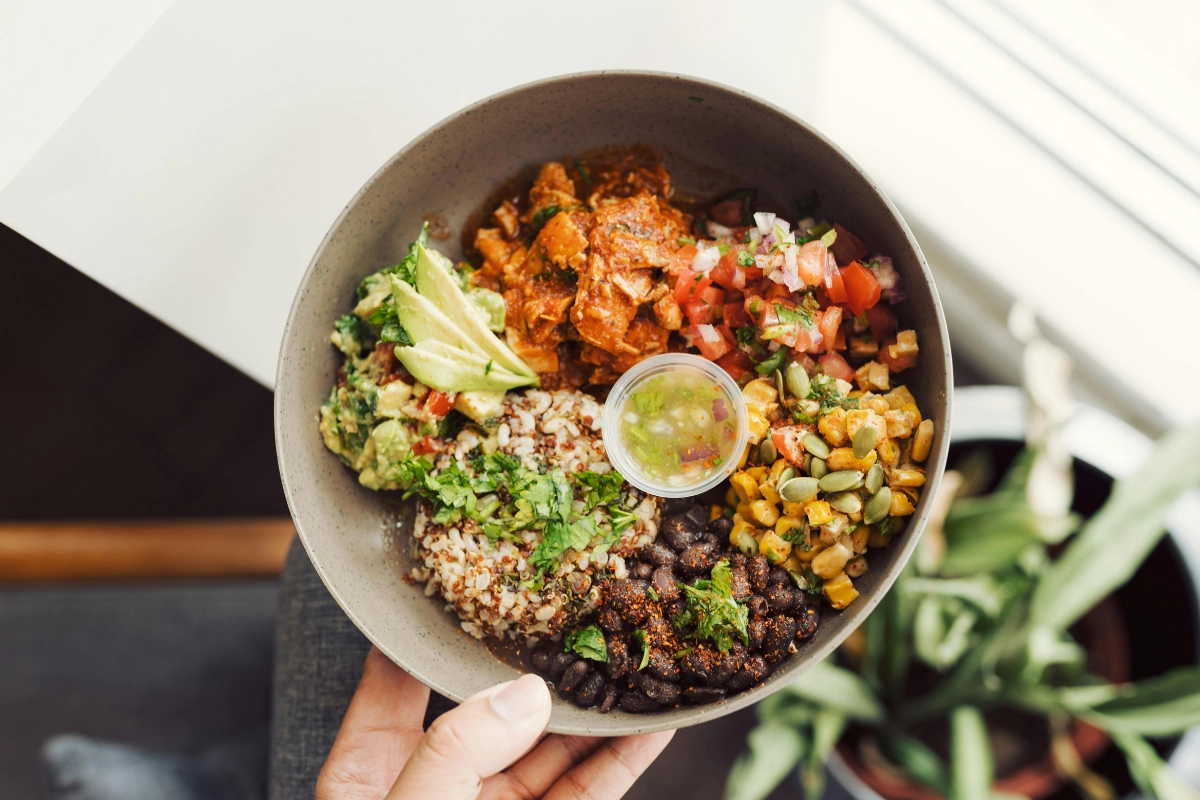 bol santé avec quinoa, haricots noirs, maïs, tomates, avocats et sauce verte.