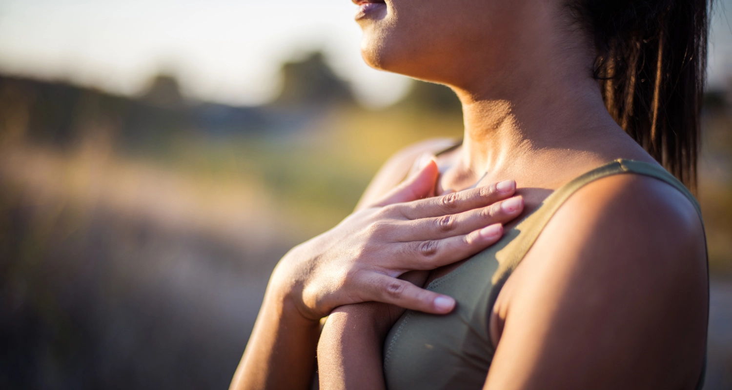 Femme, mains posées contre sa poitrine, qui fait face au soleil à l'extérieur.
