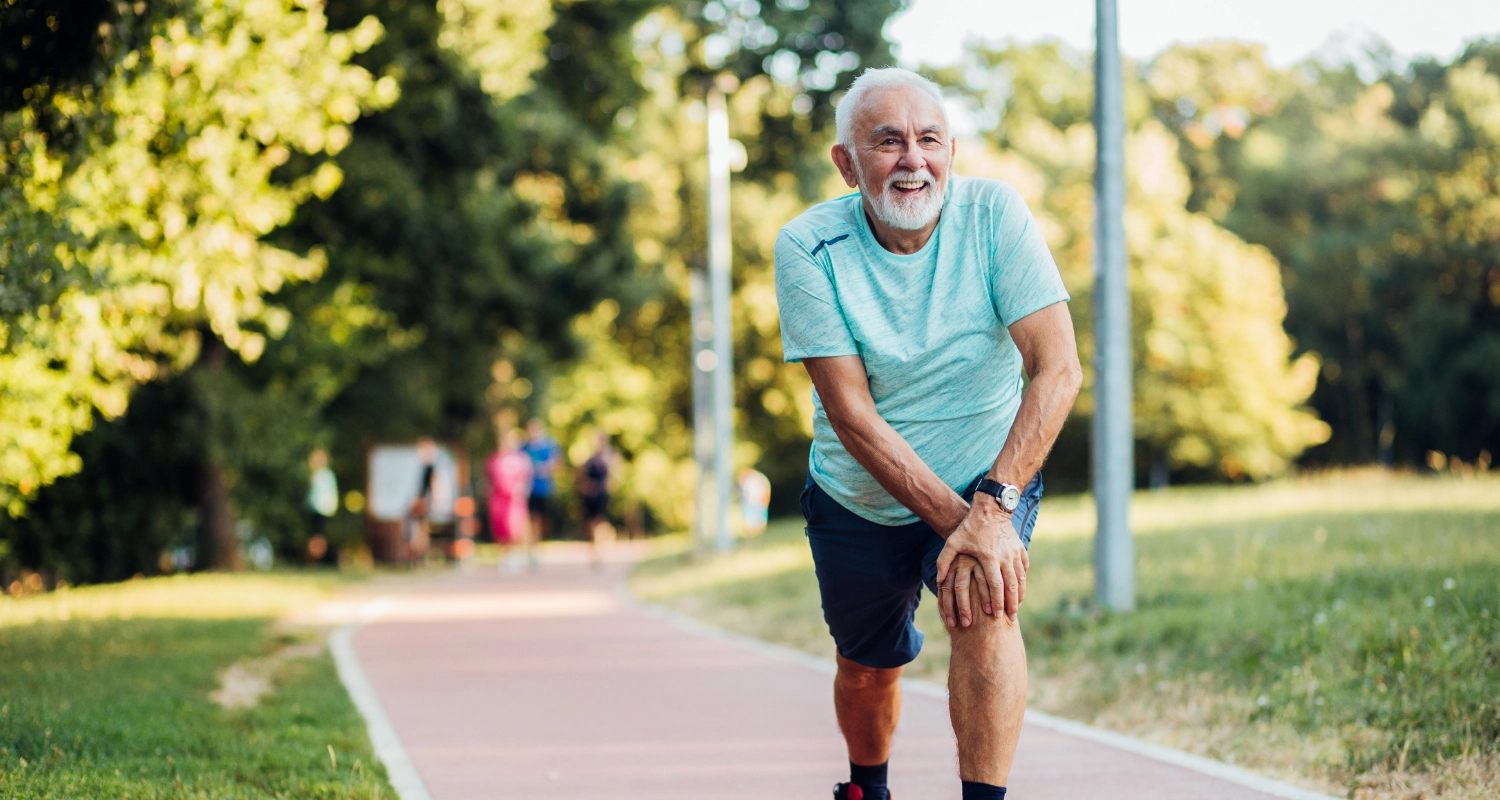 Homme âgé, souriant, habit de sport, qui se tient sur une piste de course pour joggeurs