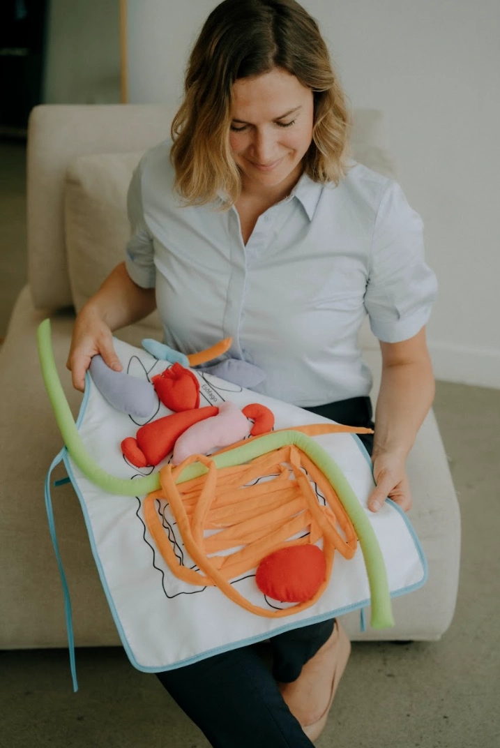 Femme qui tient un tablier qui illustre le système digestif en tissus, adapté aux enfants, matériel pédagogique
