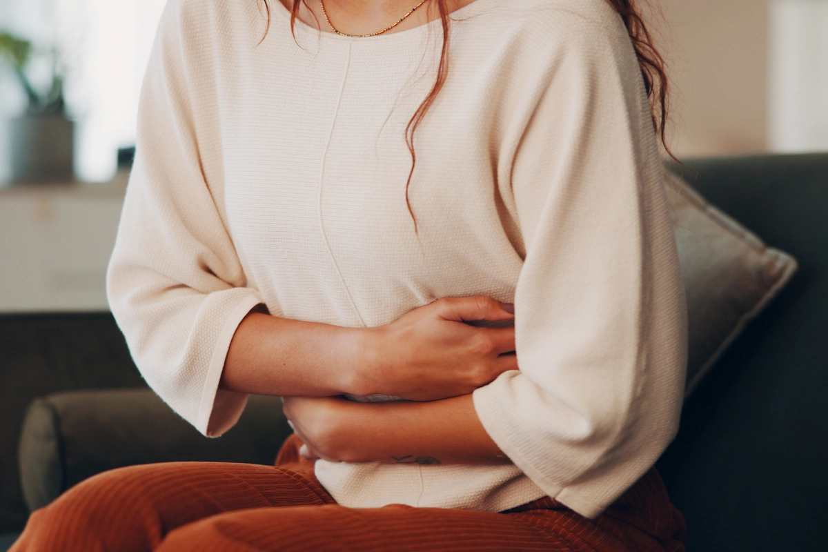 Femme qui tient son ventre, penchée légèrement vers l'avant. Elle est assise sur un fauteuil